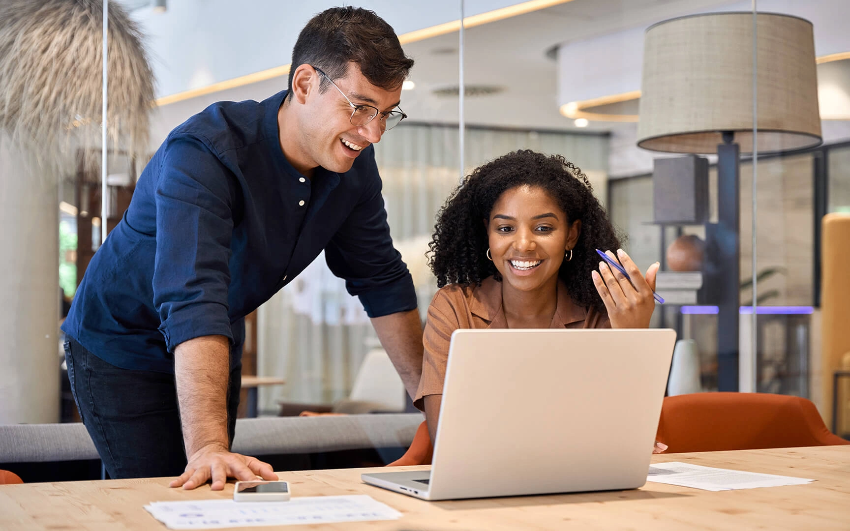 Twee professionals die samenwerken aan een bureau in een modern kantoor, documenten doornemen en inzichten bespreken terwijl ze aan een laptop werken in een lichte, eigentijdse werkruimte.