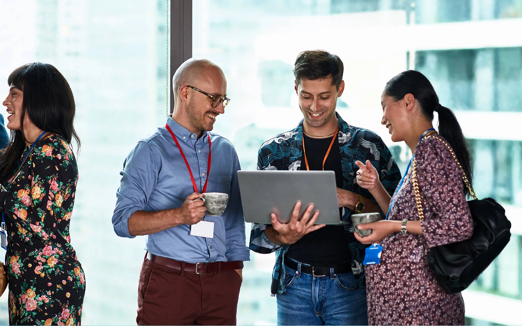 Four people gathered around a laptop, smiling and chatting in a modern office setting