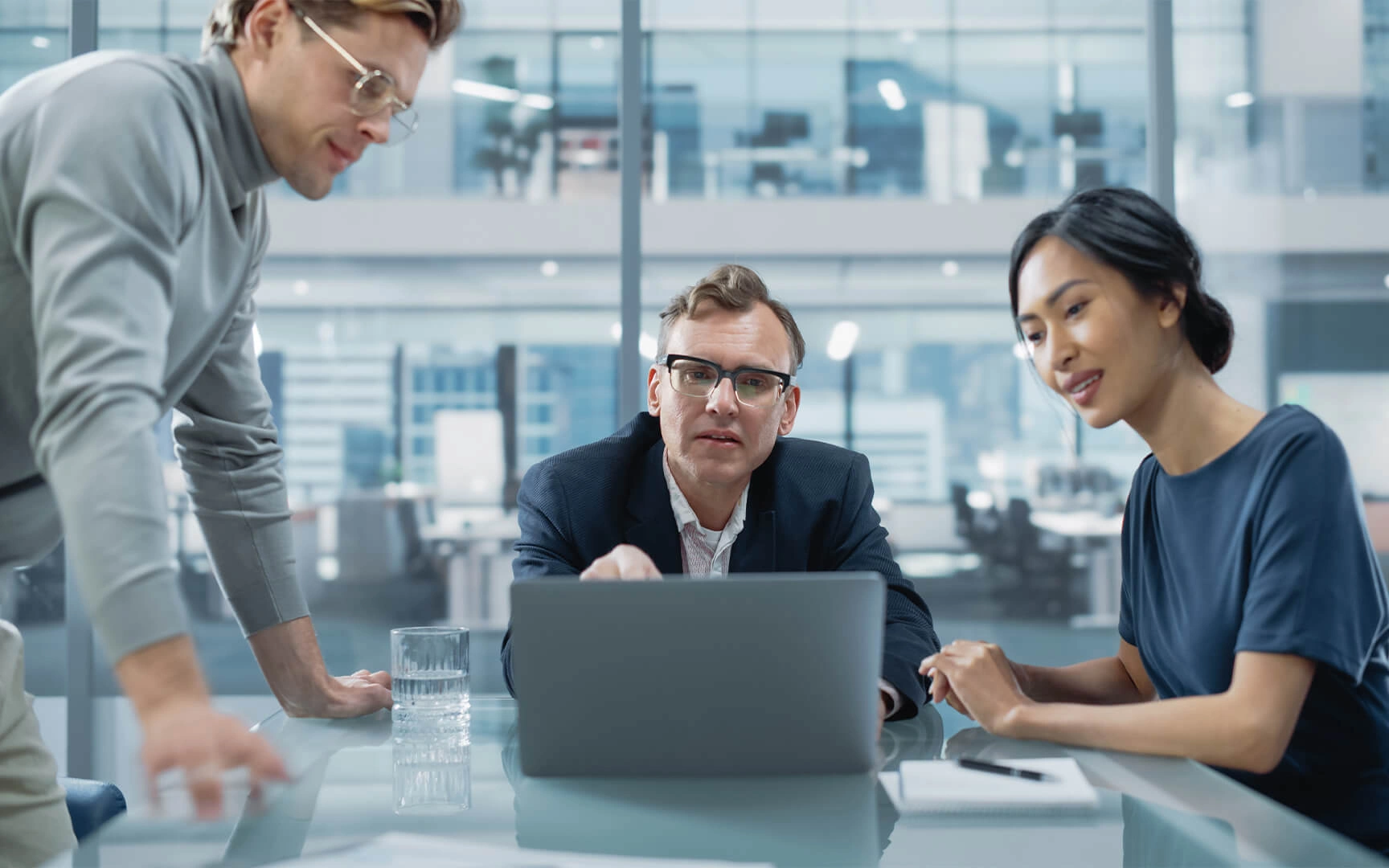 A group of professionals reviewing information on a laptop during a collaborative meeting in a modern office environment.