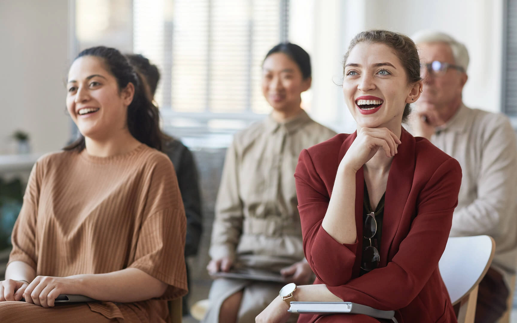 Groep professionals in een vergadering of seminar, die aandachtig luisteren en aantekeningen maken in een lichte, moderne ruimte.