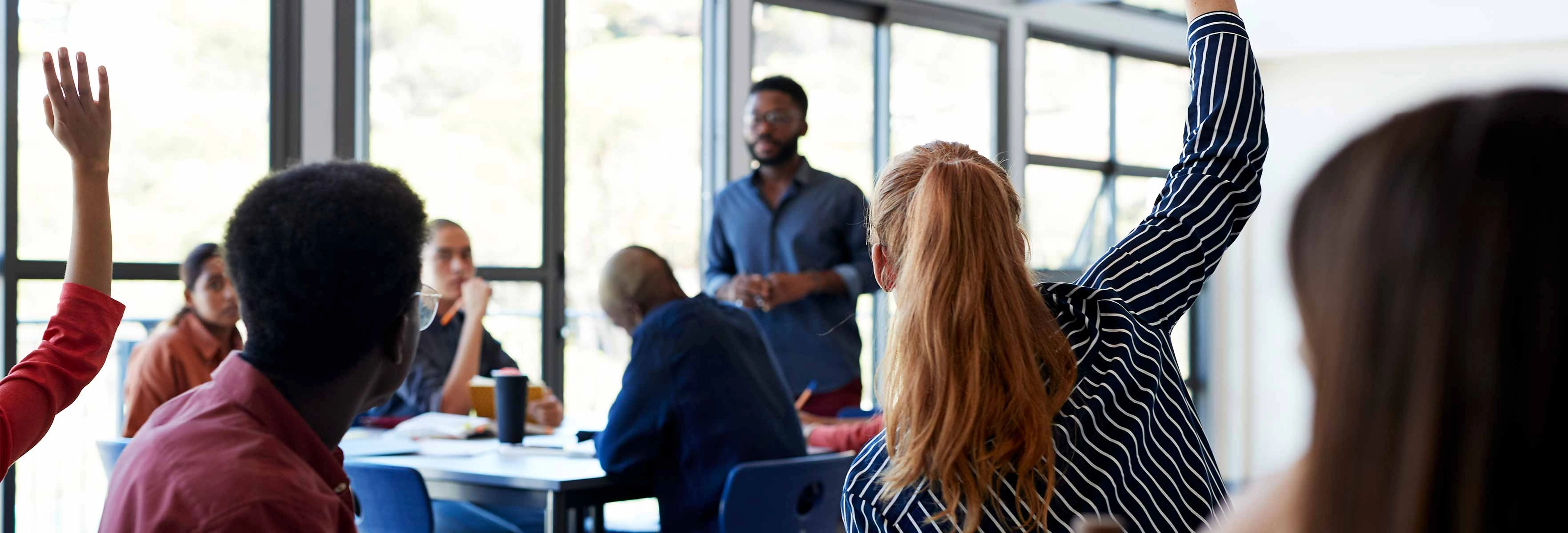 a university classroom with several students with their hands up