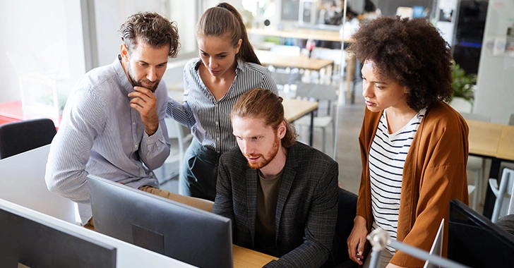 Four people gathered around a computer, looking intently at the screen in an office setting
