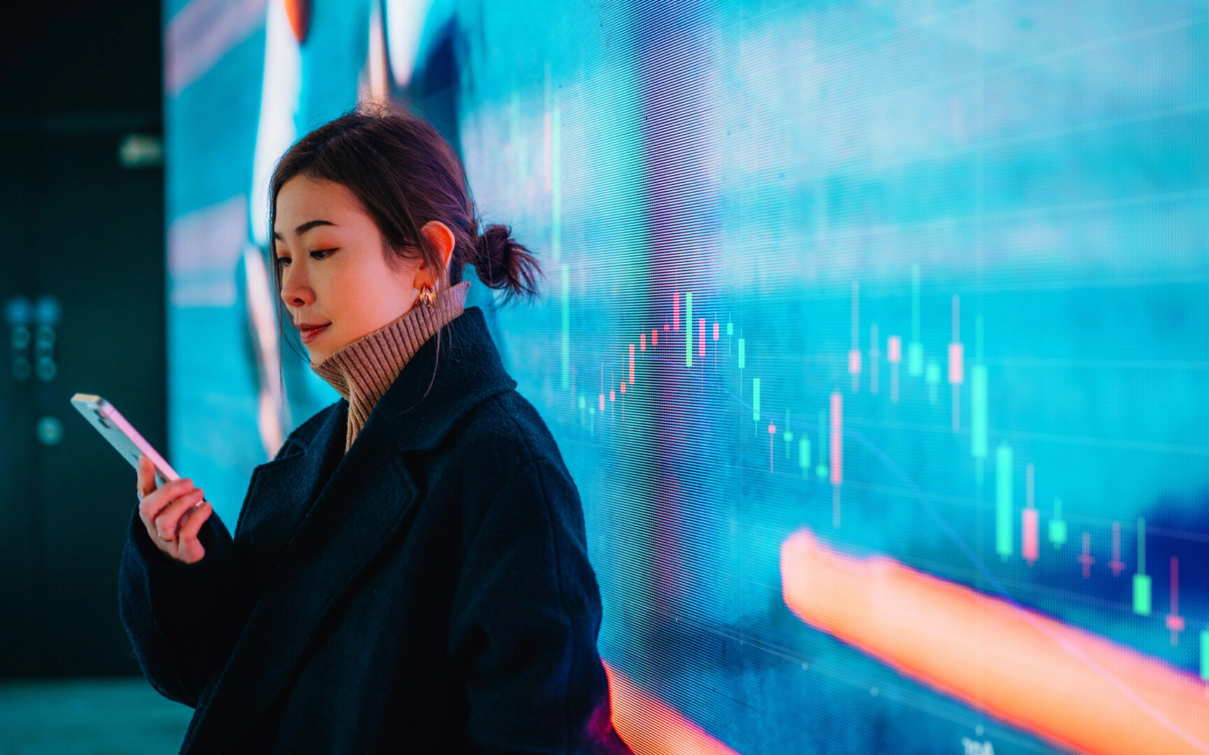 Person using a smartphone in front of a digital financial data display with charts and graphs, representing real-time analytics and FP&A insights