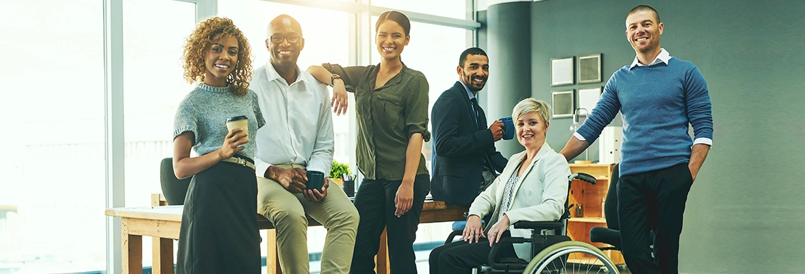 Group of six diverse professionals smiling in an office environment, one of whom is using a wheelchair.