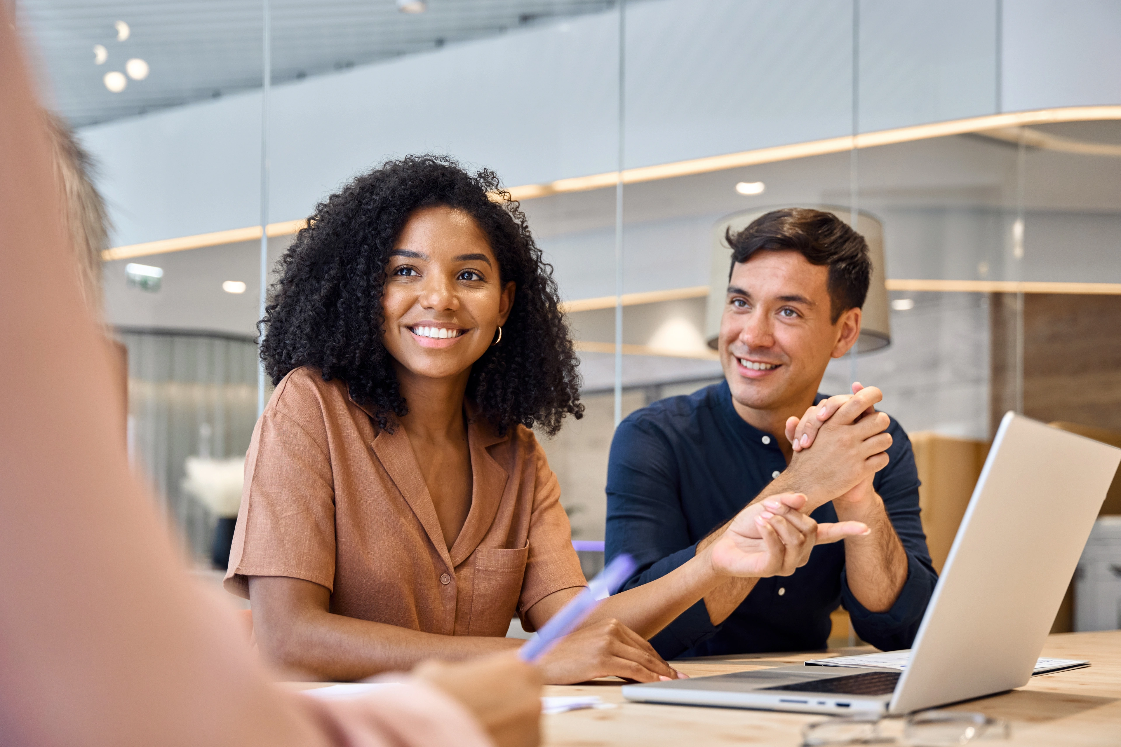 Two people in a meeting, smiling and discussing with a laptop on the table. 