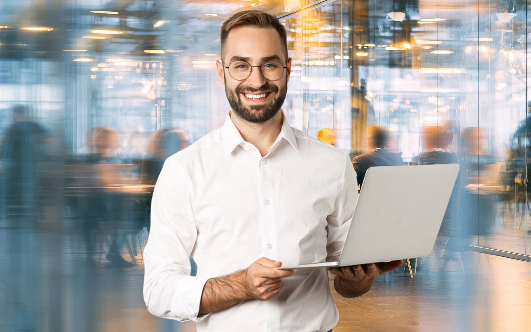 Smiling professional holding a laptop in a modern office environment with blurred colleagues working in the background