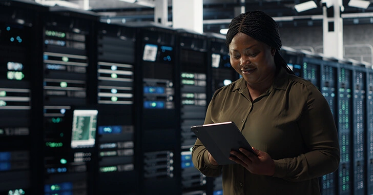 A person stands in a server room holding a tablet, surrounded by rows of server racks with glowing indicator lights.