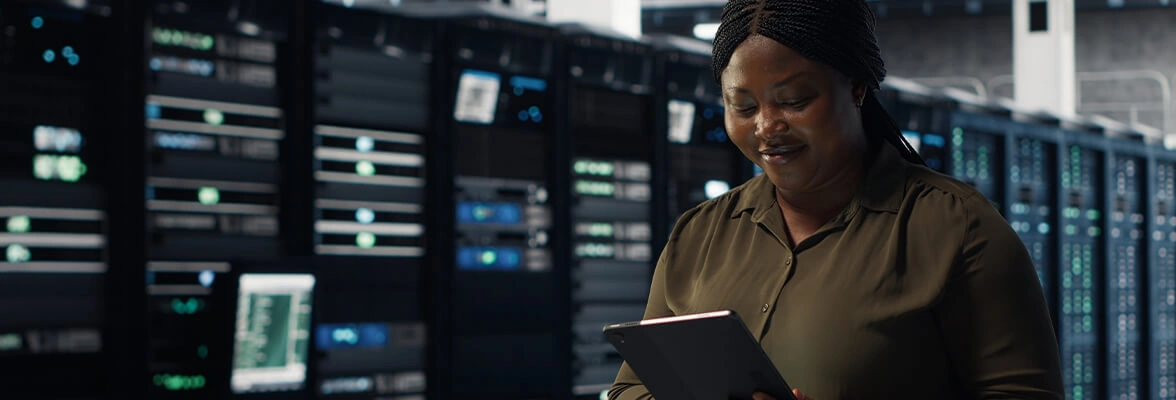 A person stands in a server room holding a tablet, surrounded by rows of server racks with glowing indicator lights.