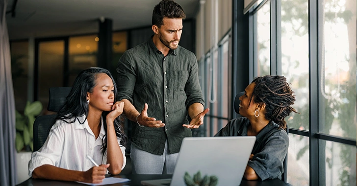 Three professionals in a discussion around a laptop in a modern office setting.