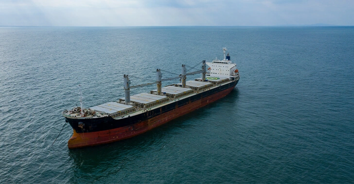 A large cargo ship sails on a vast, calm sea under a cloudy sky.