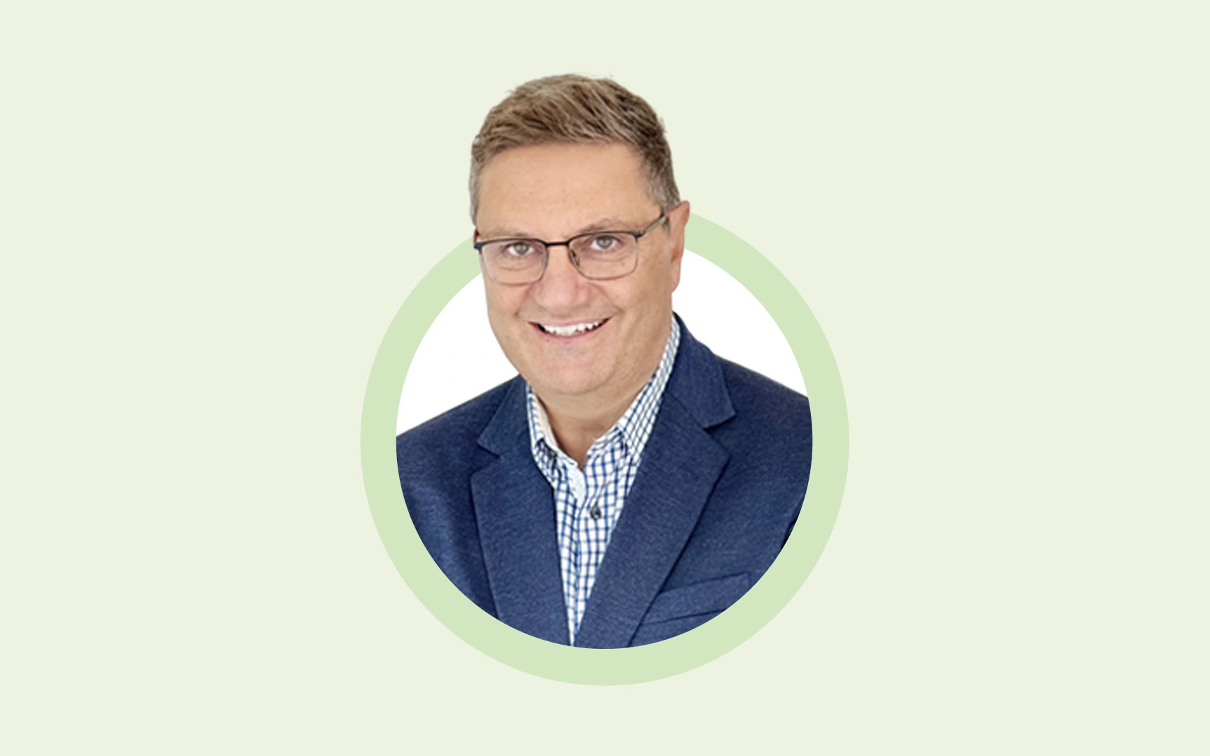 Portrait of Derek Kudsee, smiling and wearing glasses, a blue blazer, and a checkered shirt, against a light background.