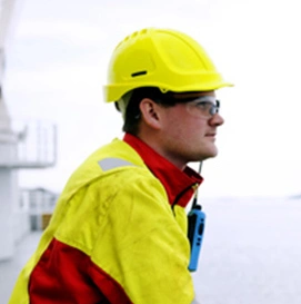 Mann i gul og rød kjeledress og gul hardhat som ser utover havet