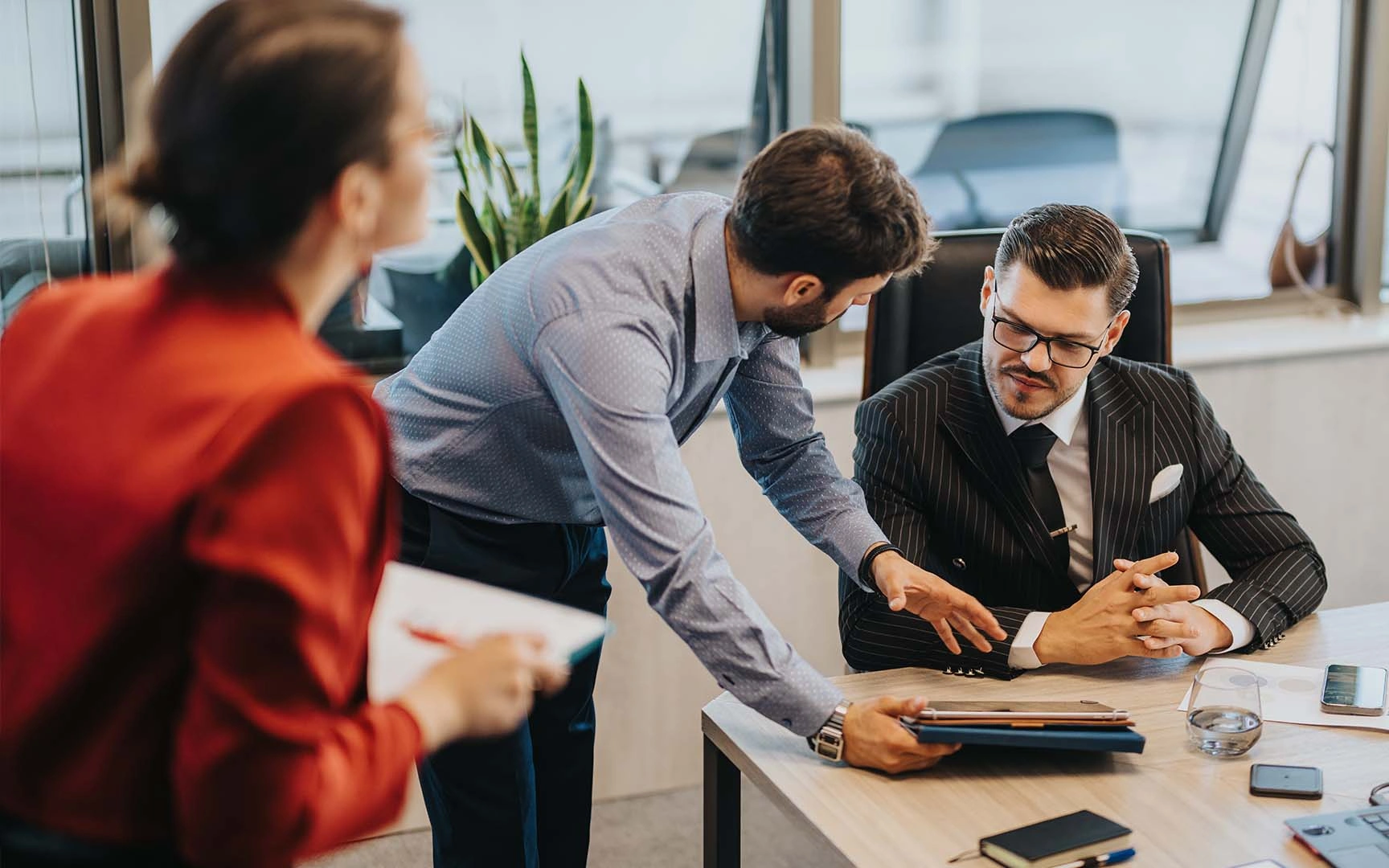 Business professionals collaborating in a modern office meeting, reviewing information on a tablet at a conference table.