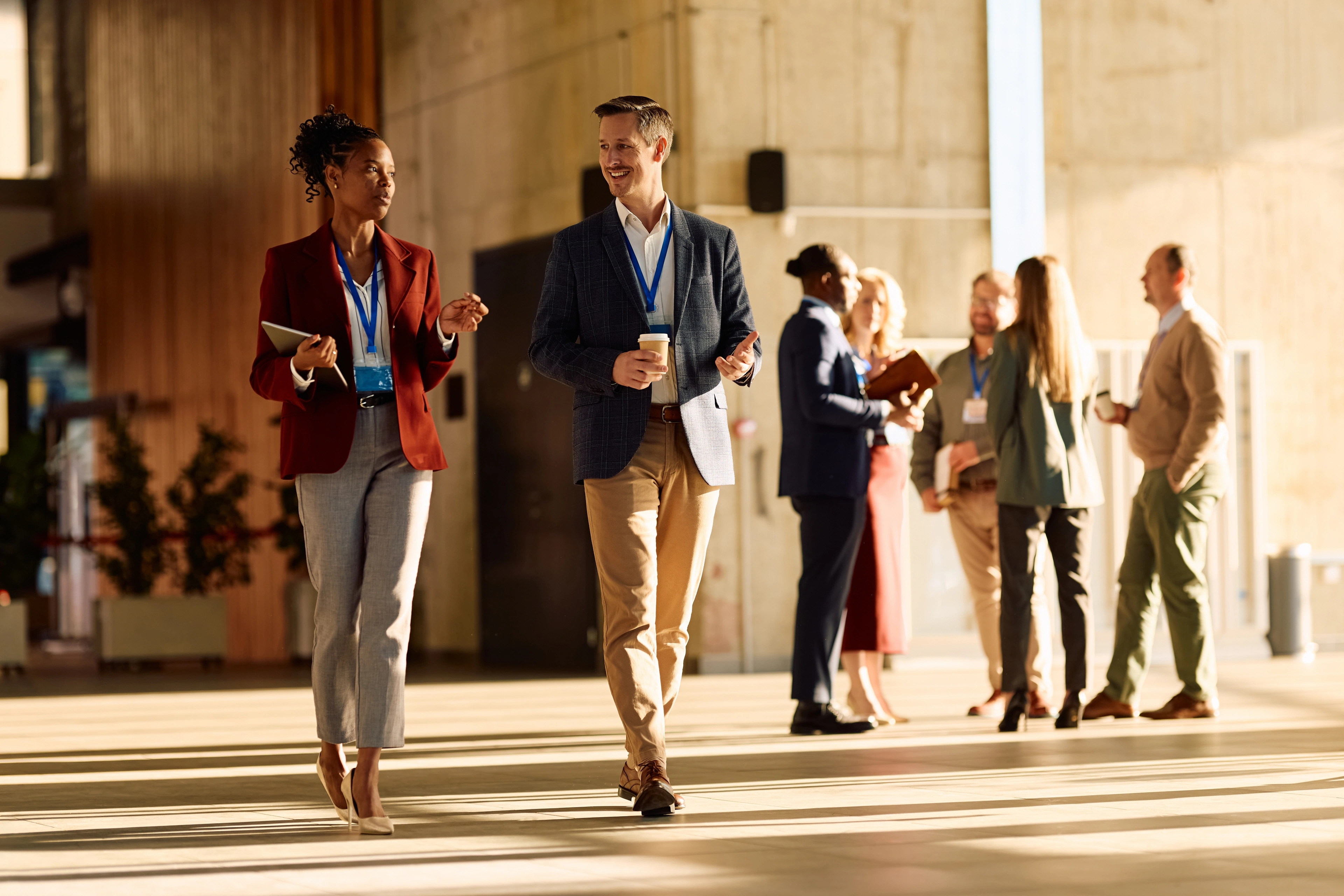 Business professionals wearing conference badges walk and network in a modern event venue.