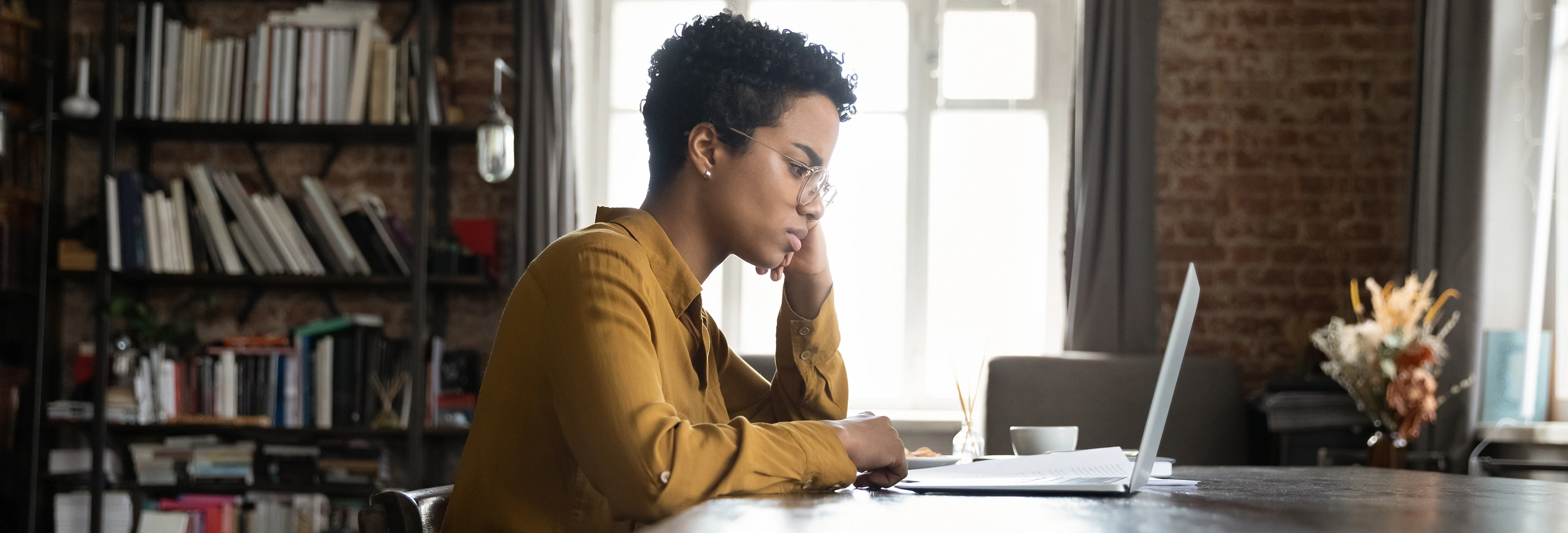 Woman sitting at at table thinking, looking at a computer