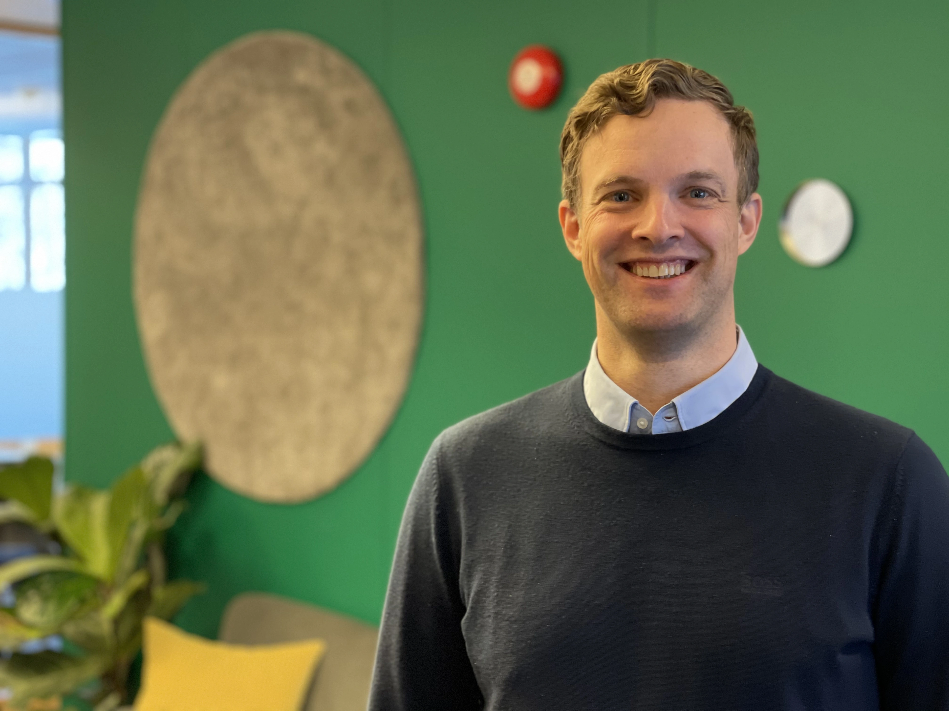 En smilende mann foran en grønn vegg