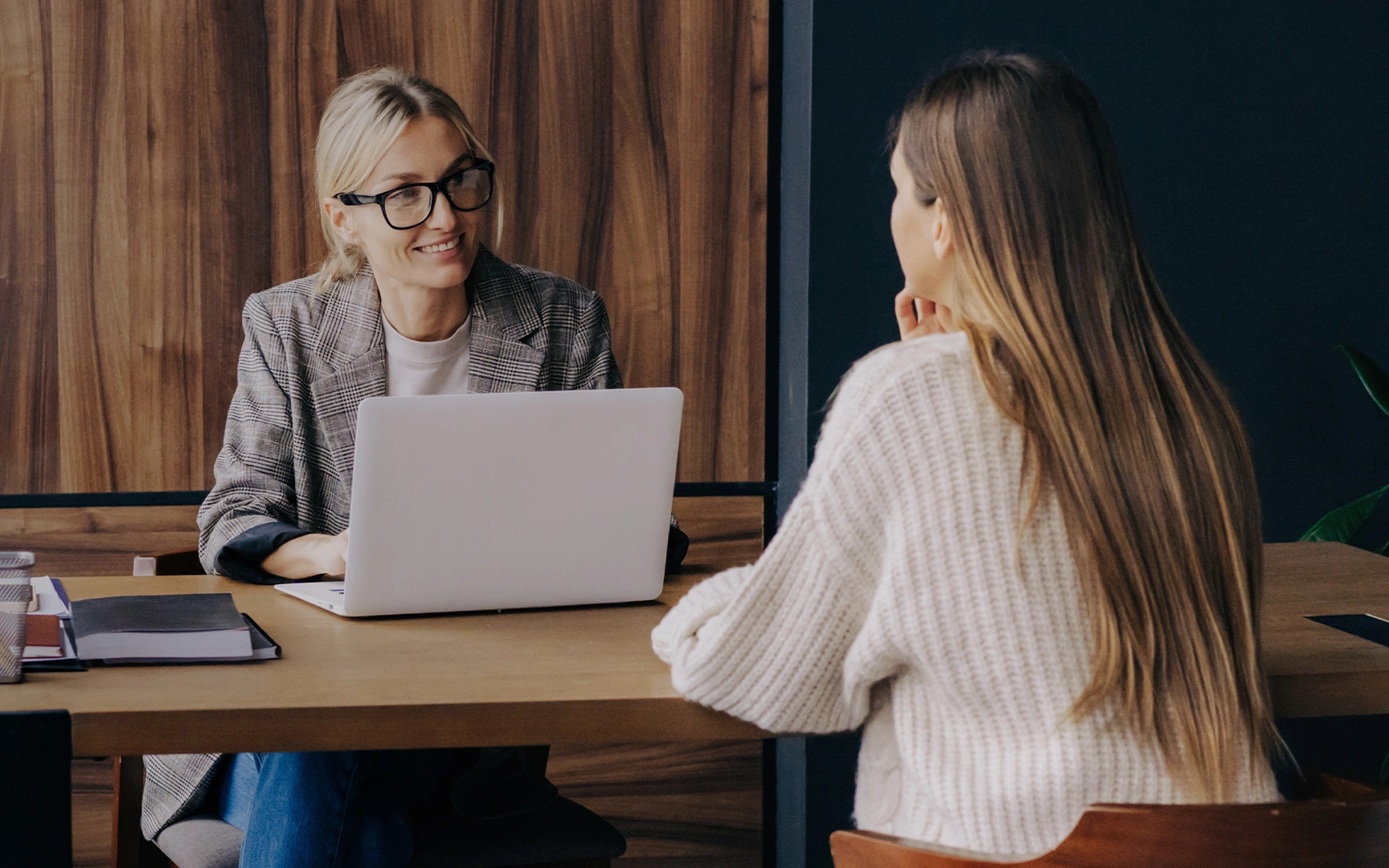 Two colleagues having a discussion across a desk with an open laptop in an office.