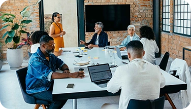 A modern office meeting with eight professionals around a sleek conference table.